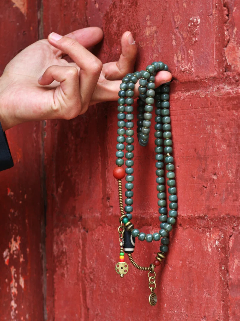 Hand holding a green beaded necklace against a red textured background
