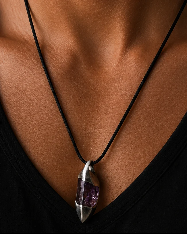 Man wearing a black shirt with a necklace featuring a purple pendant against a dark background