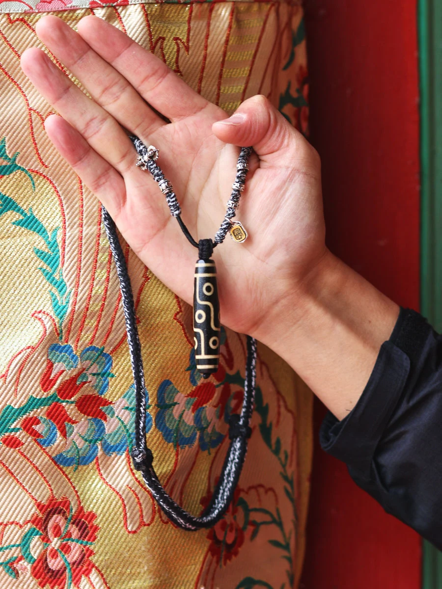 Hand holding a necklace with intricate design against a colorful fabric background