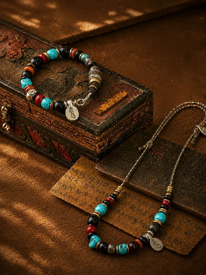 A beaded jewelry set featuring a bracelet and matching necklace with turquoise, red, black, and metallic beads, displayed on a textured brown surface next to an antique-style wooden box.