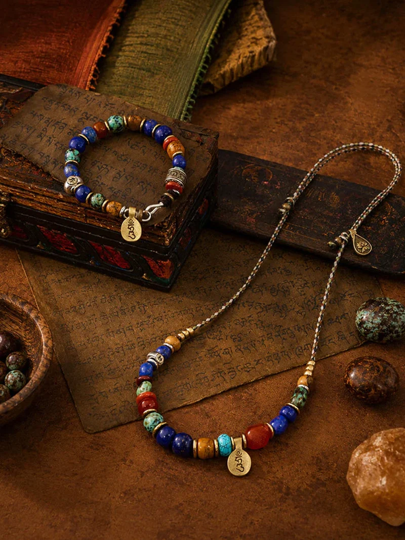 A styled flat-lay of a beaded jewelry set featuring a long necklace and a matching bracelet. The jewelry is adorned with colorful round beads in blue, red, turquoise, and brown, accented by gold-toned spacer beads and engraved round charms.