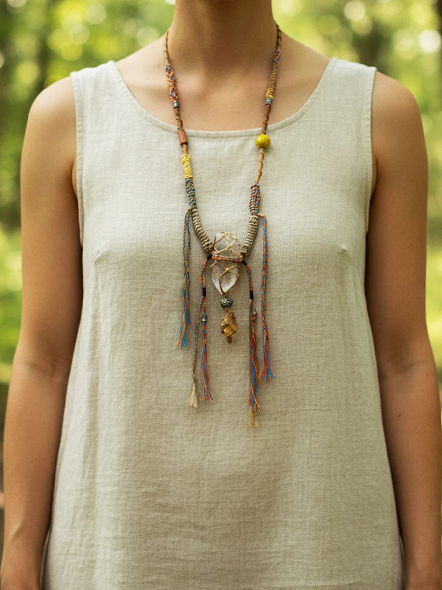 Person wearing a beige sleeveless top with a long, intricate necklace in a natural setting.